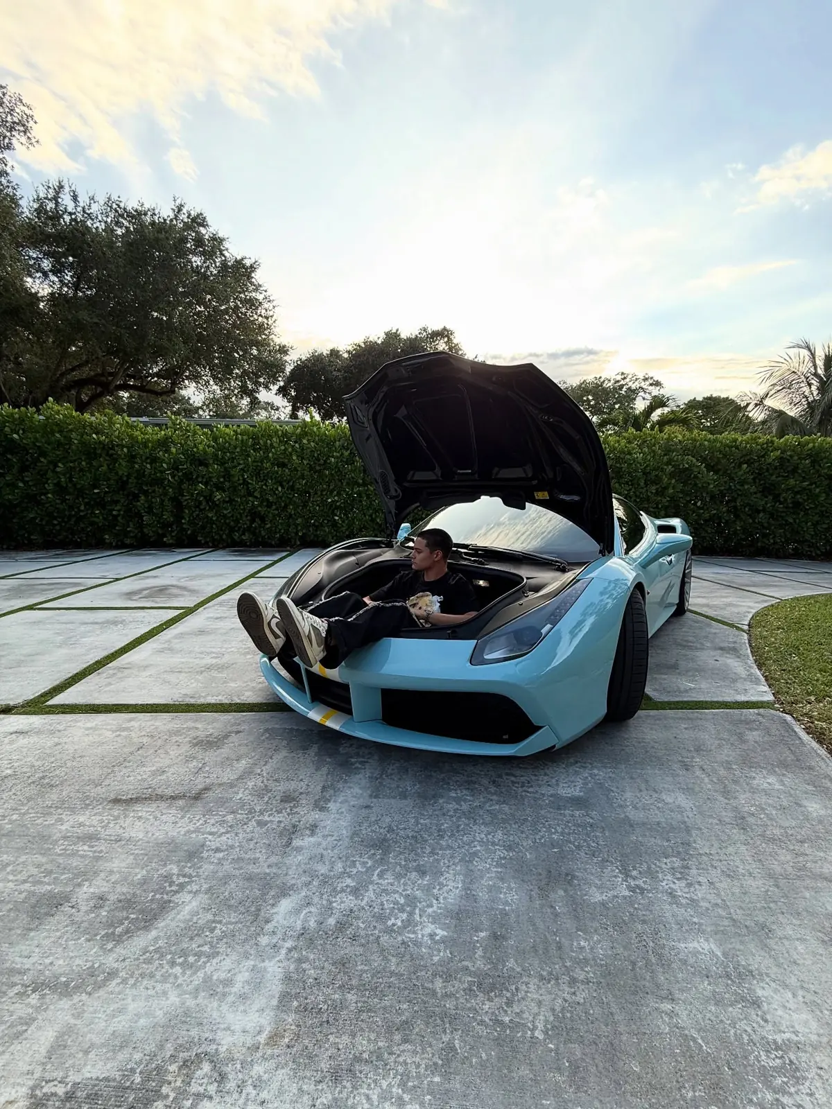 Zander sitting on the front of a light blue Ferrari with the hood open
