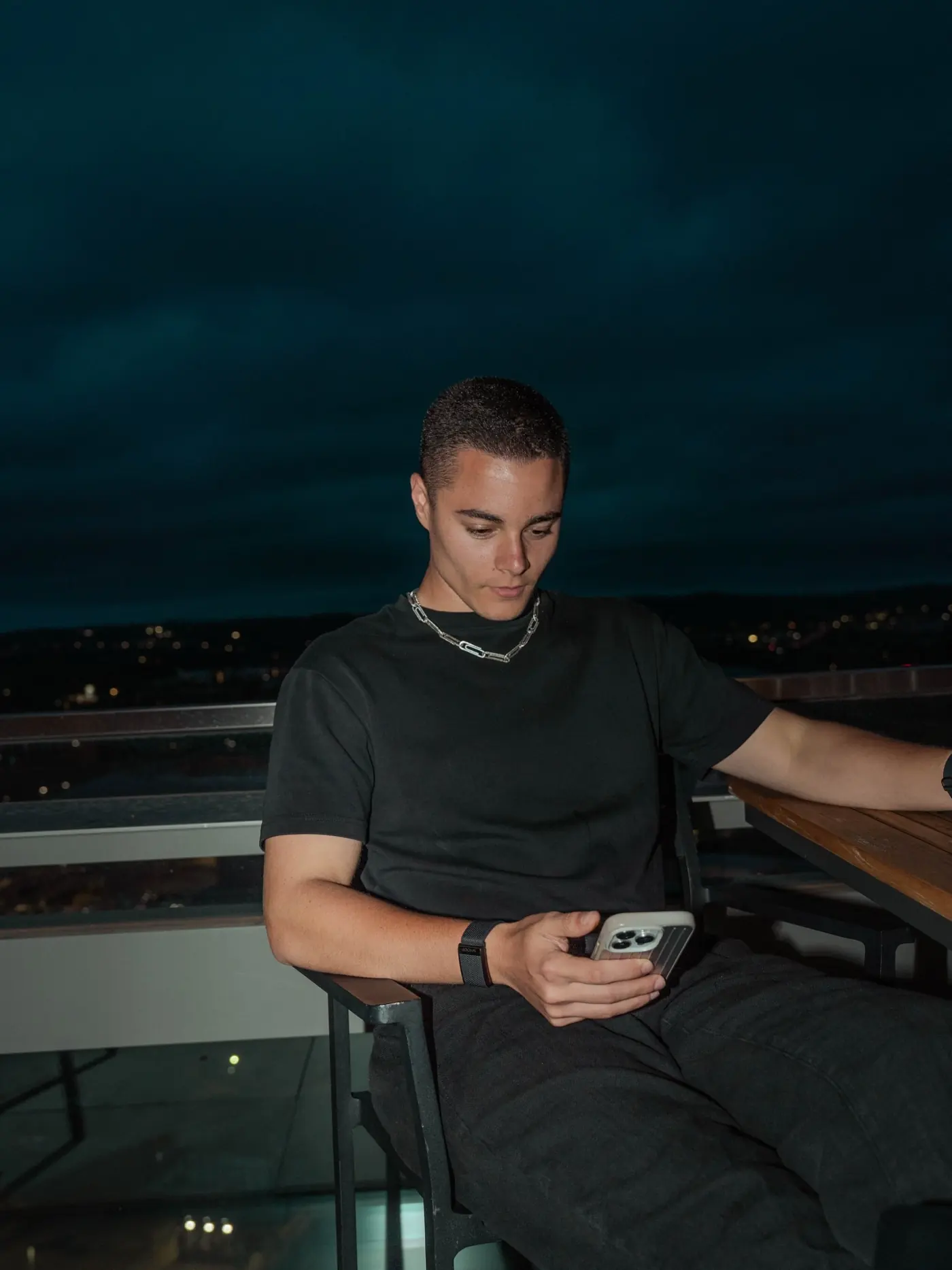 Zander checking his phone on a rooftop terrace at night